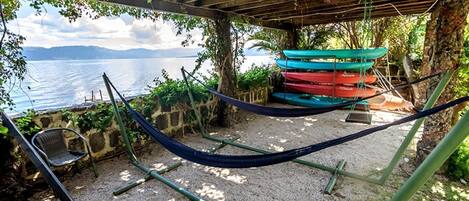 Una hamaca bajo una pérgola de madera con vistas a una playa y barcos.