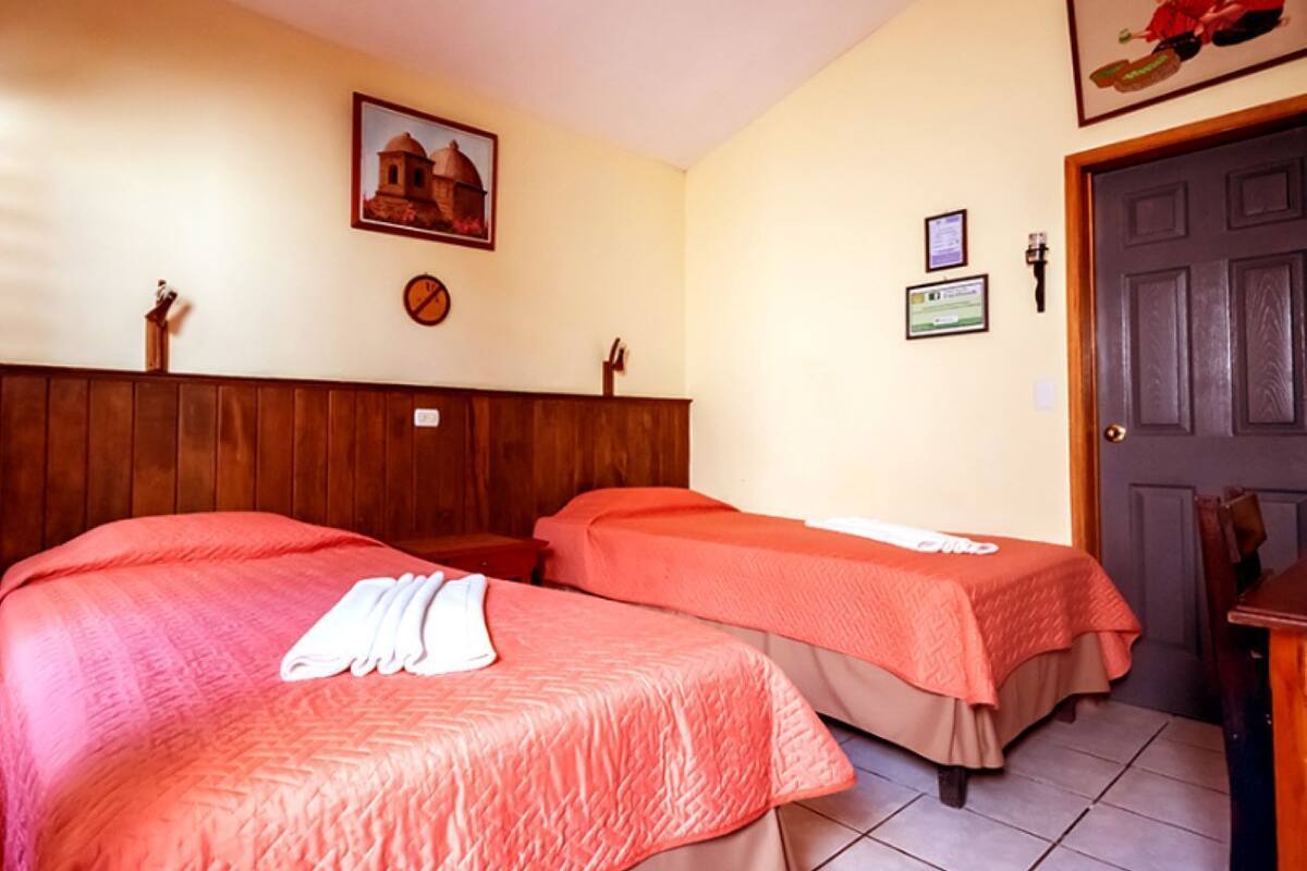 A hotel room with two beds, a wooden headboard, a door, and a wall-mounted picture.