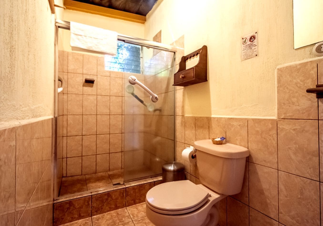 Un baño con ducha de vidrio, inodoro y un mueble de pared para artículos de tocador.