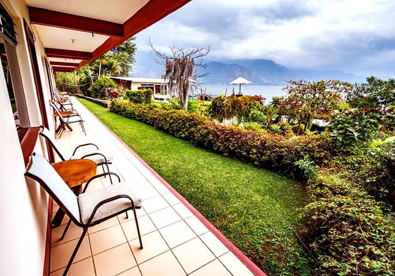 Eine Terrasse mit Sitzgelegenheiten im Freien, ein gepflegter Rasen und Blick auf Berge und ein Gewässer.