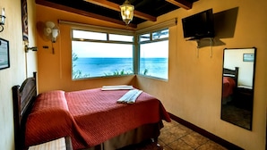 A bedroom with a bed, a window with a view of the sea, a ceiling fan, and a mounted TV. - Hotel Sak'cari El Amanecer (San Pedro La Laguna)