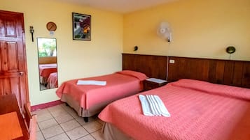 Une chambre d’hôtel avec deux lits, une porte en bois, un miroir et un ventilateur fixé au mur.