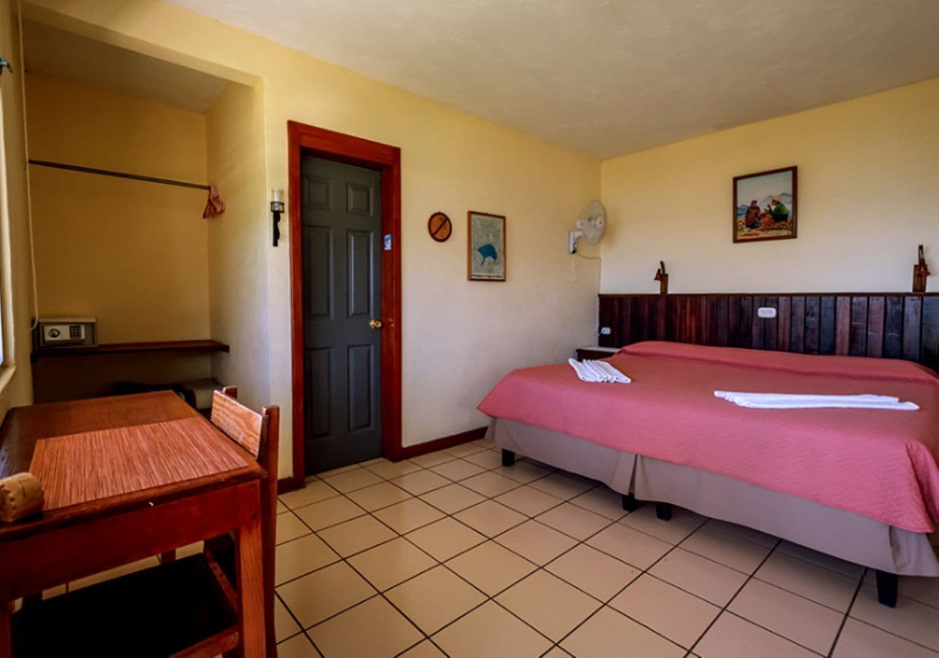 Ein Hotelzimmer mit einem Bett, einem Schreibtisch, einem Stuhl, einer Tür und einem Wandventilator.
