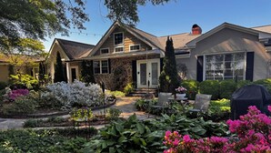 Une maison d’habitation dotée d’un porche à l’avant, d’un patio couvert et d’un jardin agrémenté de diverses plantes et fleurs.