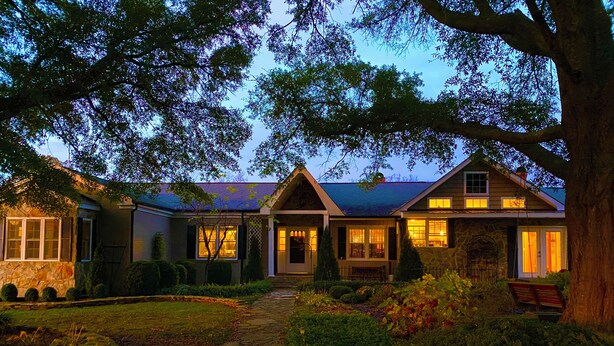 Une maison à deux étages avec une façade en pierre, un chemin en pierre menant à l’entrée et un jardin bien entretenu.