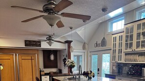 Une cuisine spacieuse dotée d’un grand îlot central, de meubles en bois et d’un ventilateur de plafond.
