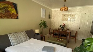 A room with a bed, a sofa, a dining table with chairs, a lamp, and a plant. - Homely 2-bed Apartment - Sleeps 3 & Parking (Walton-on-Thames)