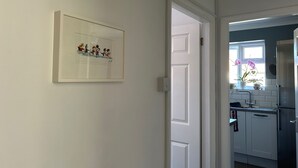 A hallway with a white door leading to a kitchen area. - Homely 2-bed Apartment - Sleeps 3 & Parking (Walton-on-Thames)