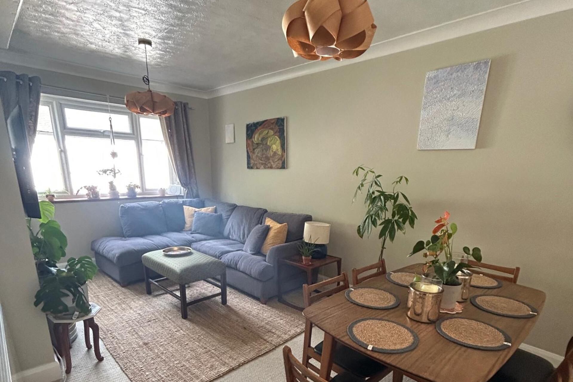 A living room with a blue sofa, a dining table with placemats, and a hanging light fixture.