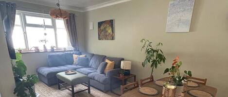 A living room with a blue sofa, a dining table with placemats, and a hanging light fixture.
