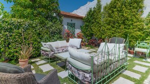 Une terrasse avec des meubles d’extérieur, un cadre de lit en métal vert et un mur blanc surmonté d’un toit en tuiles.