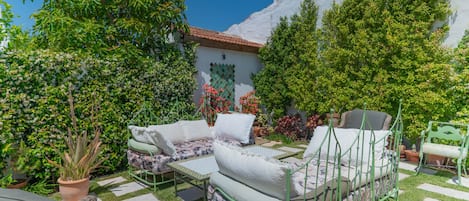 A patio with outdoor furniture, a green metal bed frame, and a white wall with a tiled roof.