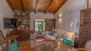 Un salon chaleureux avec un plafond en bois, un téléviseur, une table à manger agrémentée d’un plateau décoratif et un canapé avec des coussins colorés.