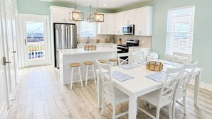 Een ruime keuken met witte kasten, een centraal eiland en een eetgedeelte met witte stoelen en een tafel.
