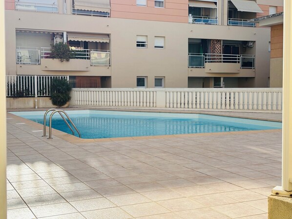 Una piscina con bordeado de baldosas, rodeada por una barandilla blanca y un muro bajo.