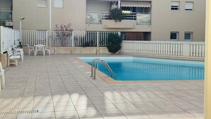 A swimming pool with a tiled deck, white chairs, and a white fence.