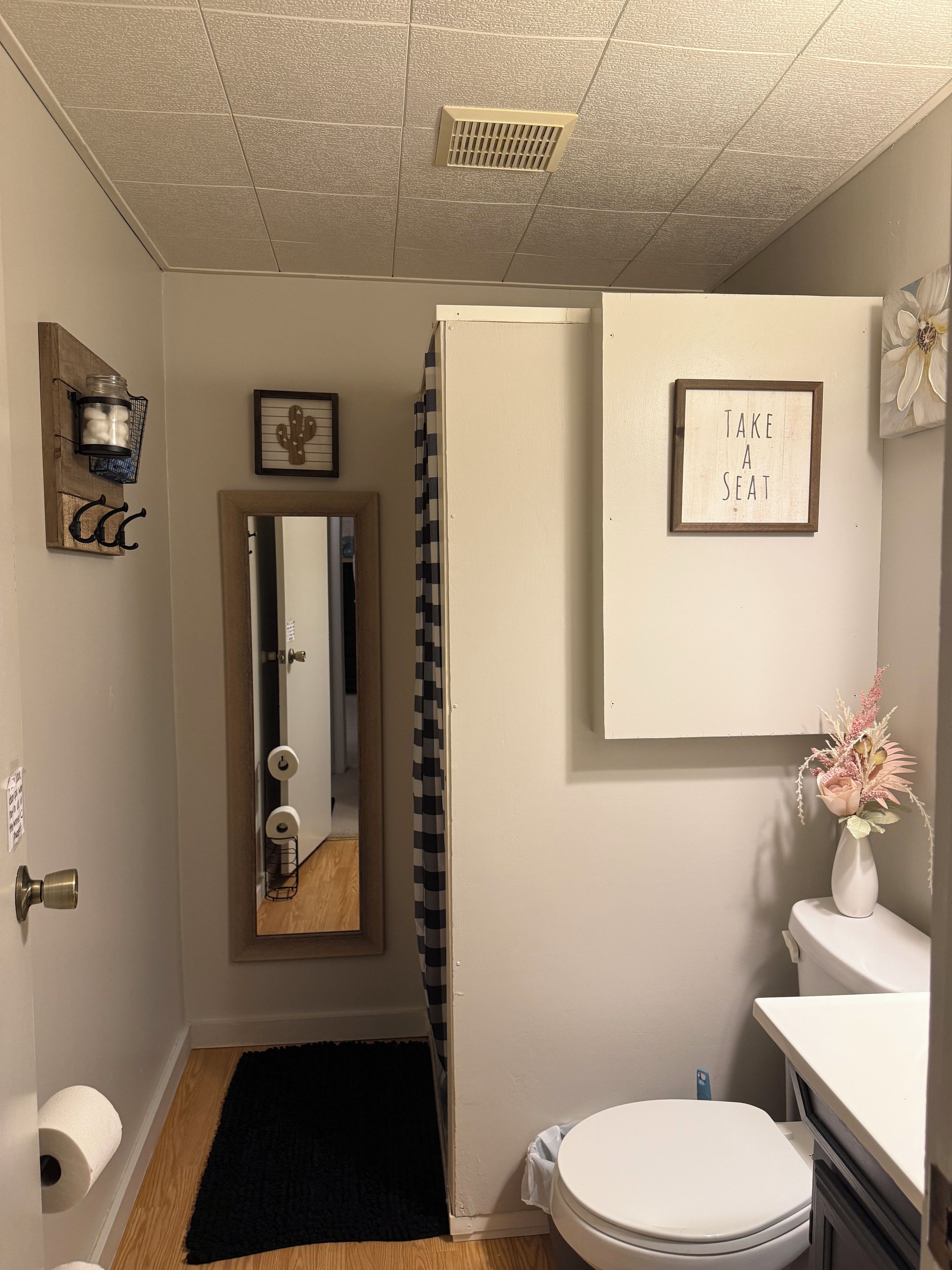 Une salle de bain comprenant des toilettes, un lavabo, un miroir, un rideau de douche et un panneau encadré accroché au mur.