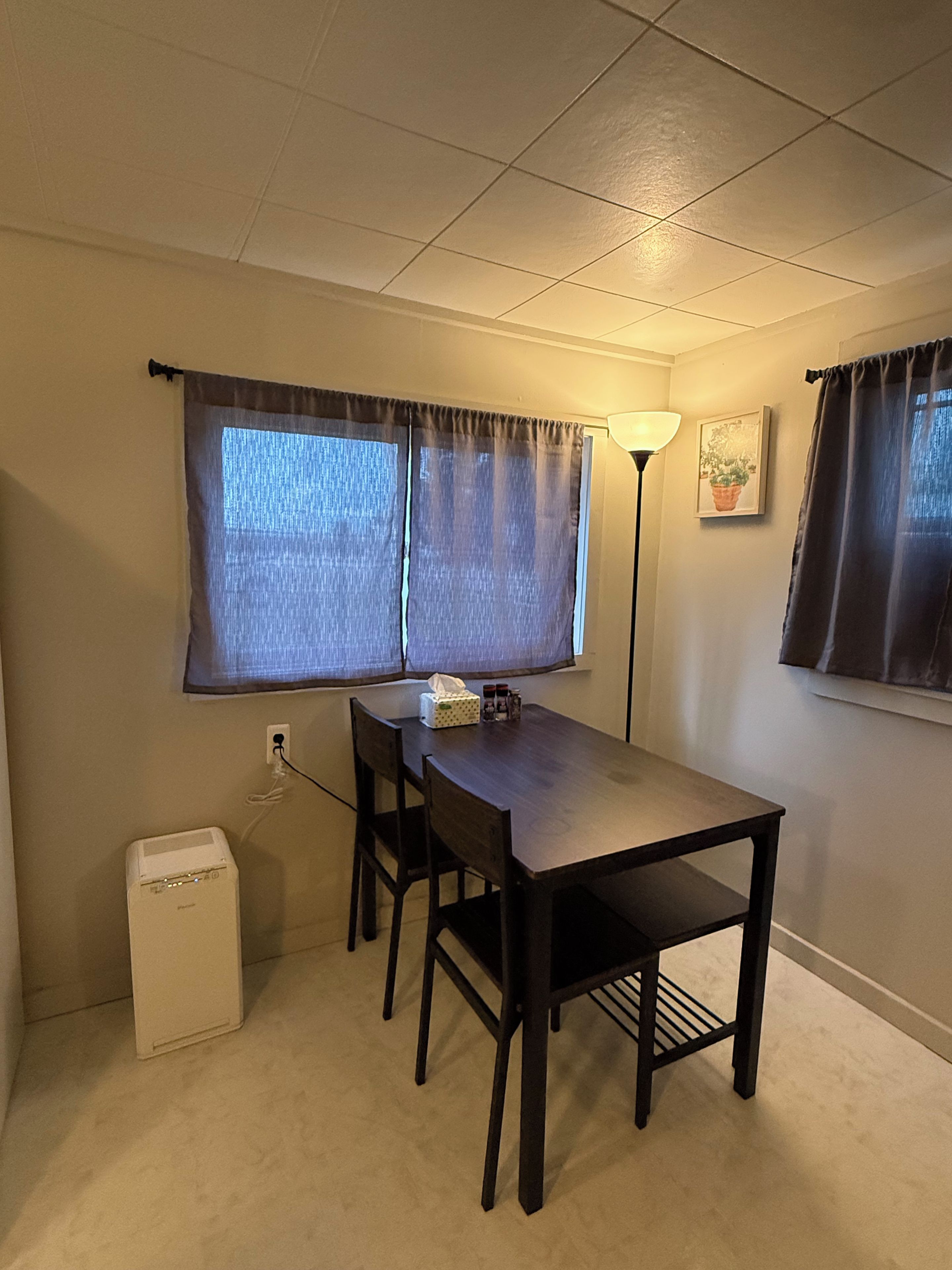 A room with a wooden table and two chairs, a lamp, and a window with curtains.