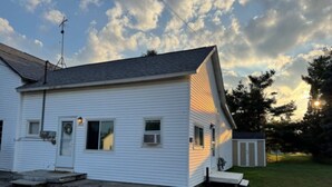 A single-story house with a front porch, a small attached garage, and a clear sky with clouds.