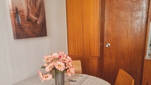 Un comedor con una mesa cubierta por un mantel a rayas, sillas, un jarrón con flores y un aparador de madera.
