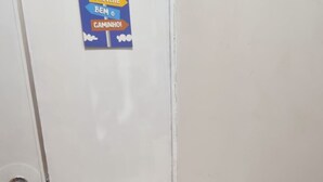 Un refrigerador blanco y compacto con un pequeño logotipo, una puerta con manija y un cartel en la pared encima.