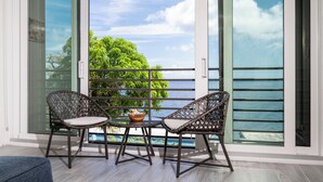 A balcony with wicker chairs and a table, overlooking a body of water and greenery. - New central located 2BR/3BD/2BA condo gated community with 2 pools & pickleball (St Thomas)