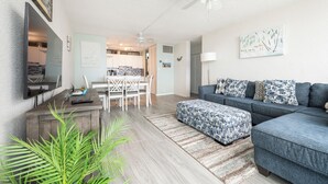 A modern living room with a grey sofa, patterned ottoman, and a dining area with white chairs and a table. - New central located 2BR/3BD/2BA condo gated community with 2 pools & pickleball (St Thomas)