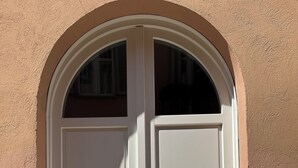 Une porte à deux battants, dotée d’un cadre blanc et d’une petite fenêtre au-dessus, le tout encastré dans un mur de couleur beige.