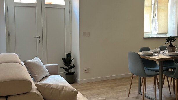 Un salon moderne avec un canapé, une table à manger et des chaises, une plante en pot et une grande porte en arc de cercle.