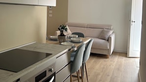 Une cuisine moderne dotée d’une cuisinière et d’un four intégrés, un coin repas avec une table et des chaises, et un canapé à l’arrière-plan.
