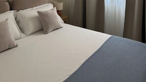 Un lit bien fait, agrémenté de plusieurs oreillers, une lampe de chevet et une fenêtre avec des rideaux légers.