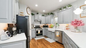 A modern kitchen with grey cabinets, stainless steel appliances, and a wooden floor. - Family-Friendly 5BR Home w/ Games & Massage Chair (Papillion)