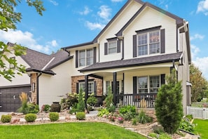 A two-story house with a covered porch, a stone foundation, and a well-maintained garden. - Family-Friendly 5BR Home w/ Games & Massage Chair (Papillion)