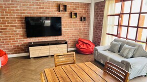 Un salón con pared de ladrillo, un televisor de pantalla plana, un sofá, una mesa de madera y un sillón de peluche rojo.