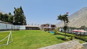 Zona verde con piscina, un edificio con balcón y una montaña al fondo.