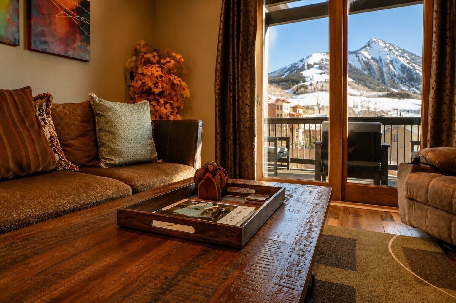 A living room with a wooden coffee table, a sofa, and a view of a mountain through a large window.