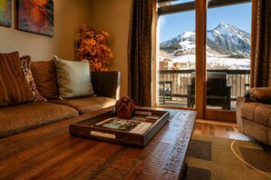 Ein Wohnzimmer mit Couch, Holztisch und Blick auf einen Berg durch ein großes Fenster.