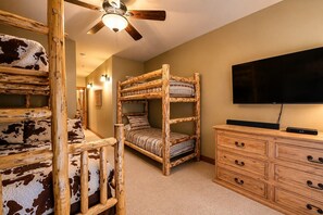 A room with a bunk bed, a ceiling fan, a television, and a wooden dresser.