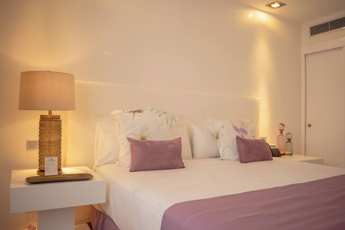 Une chambre d’hôtel avec un lit, une table de chevet avec une lampe et une petite table de nuit avec un téléphone et une bouteille.