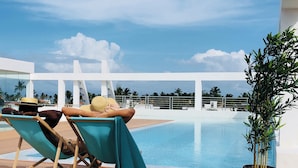 Un espace aménagé au bord de la piscine, avec deux chaises longues, un pot de fleurs et une vue sur la piscine et les palmiers.
