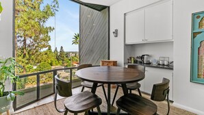 A modern kitchen with white cabinets, a round dining table, and a view of trees through large windows. - Sherman Oaks Oasis with Views and Pool Table (Los Angeles)
