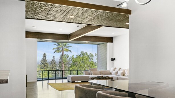 A modern living room with a glass dining table, a sofa, and a view of palm trees and mountains. - Sherman Oaks Oasis with Views and Pool Table (Los Angeles)