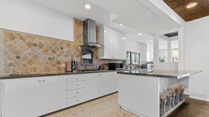A modern kitchen with white cabinets, a granite countertop, a built-in oven, and a backsplash with a geometric pattern. - Sherman Oaks Oasis with Views and Pool Table (Los Angeles)