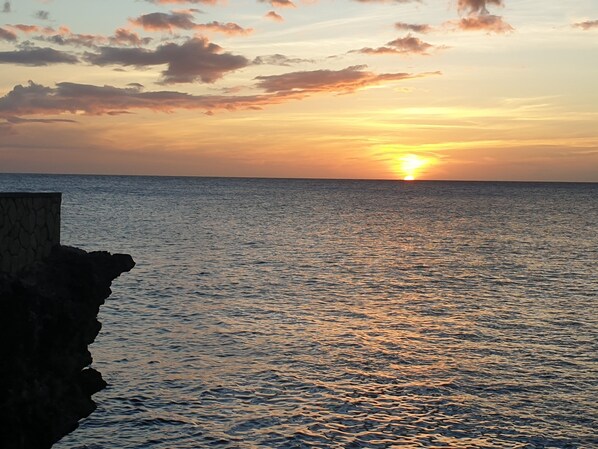 A sunset over the ocean with a rocky coastline. - Premier Oceanfront Condo Escape in West End Negril (Negril)