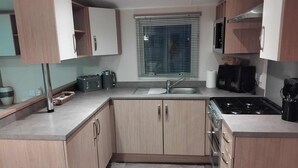 Una cocina compacta con armarios de madera, estufa integrada, lavamanos y ventana con persianas.