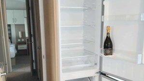 Un refrigerador abierto con varias estantes y una botella de champán en el estante superior.