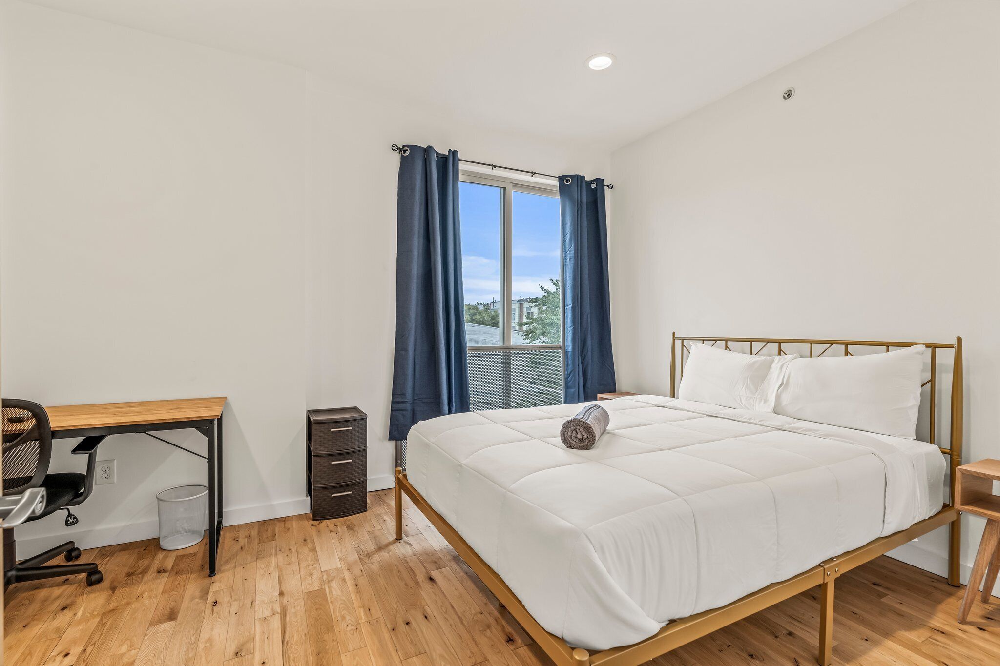 A bedroom with a bed, a desk, and a window with curtains.