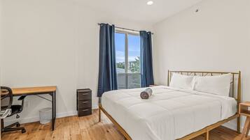 A bedroom with a bed, a desk, and a window with curtains.