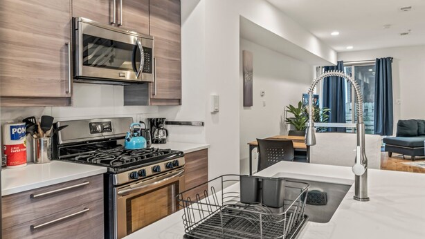 A modern kitchen with stainless steel appliances, wooden cabinets, and a central island with a sink and dish rack.