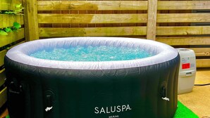 A black inflatable hot tub labeled SALUSPA MIAMI, placed on a green surface with a wooden fence and buildings in the background.